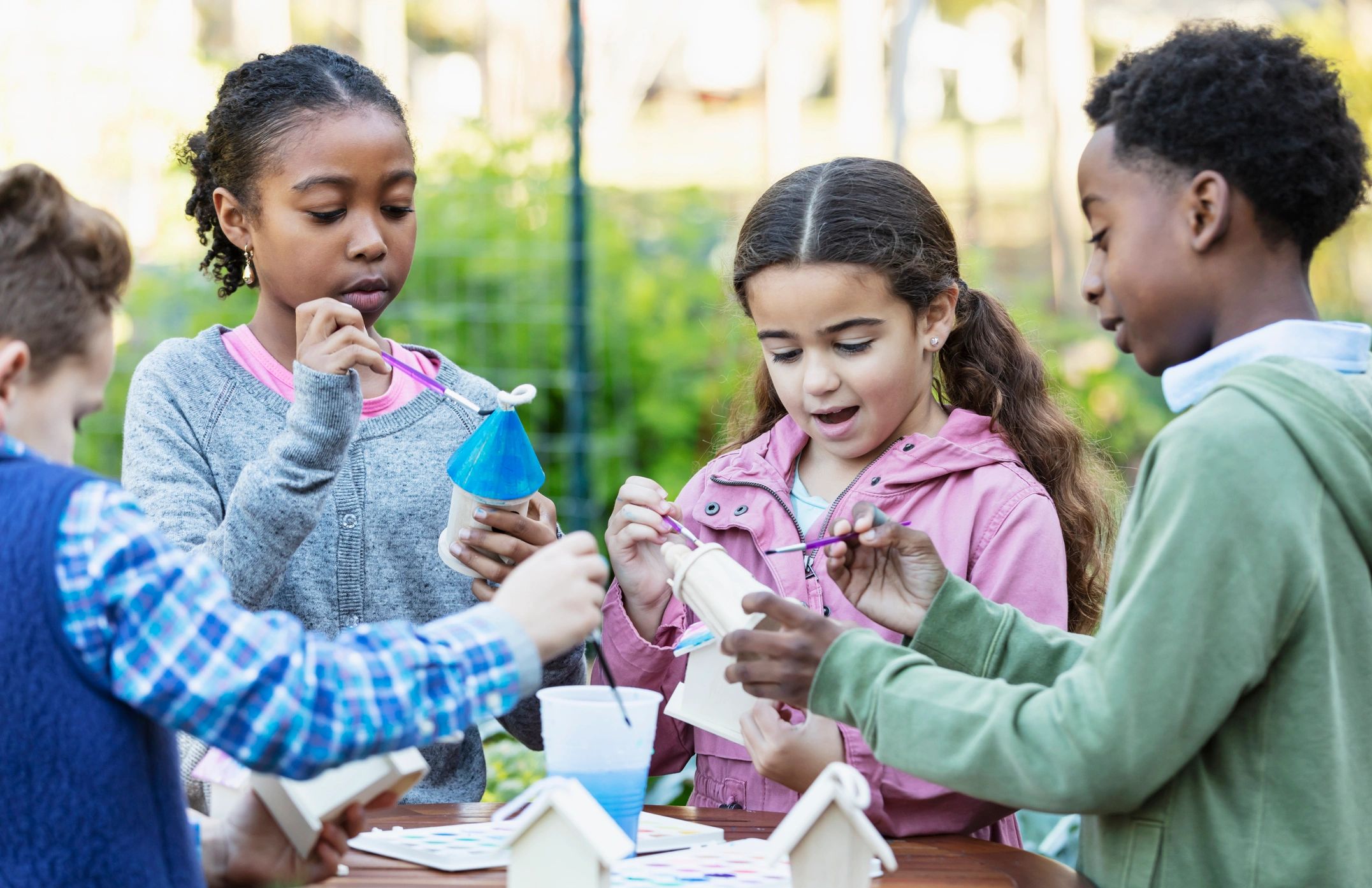Kids painting birdhouses together outdoors