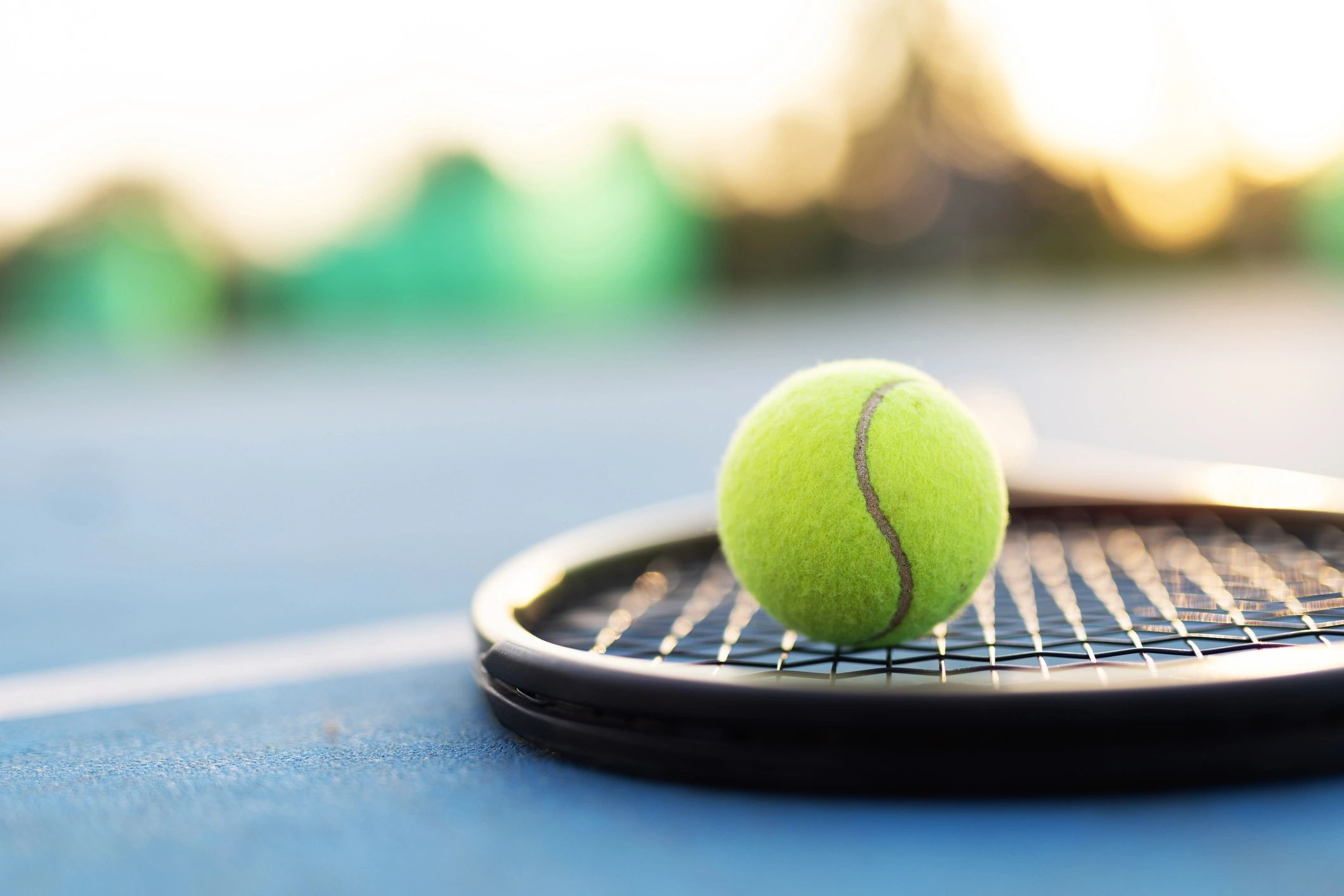 Closeup of a tennis racket and ball on a blue court surface