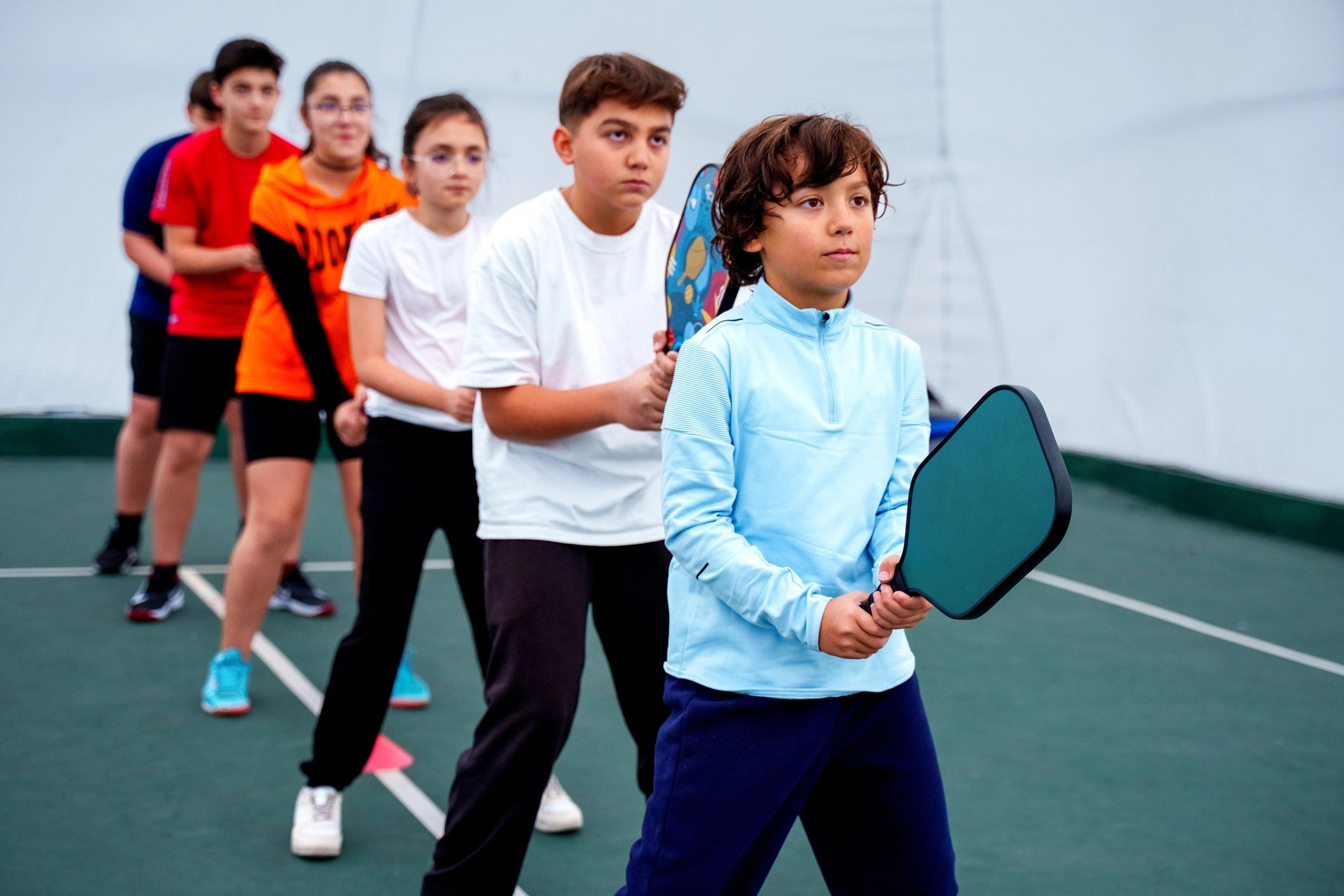 Kids practicing a racket sport indoors with a coach