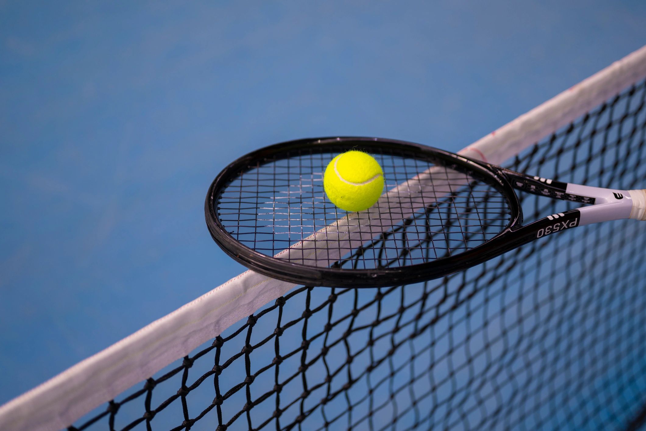 Tennis player balancing a ball on a racket at the net