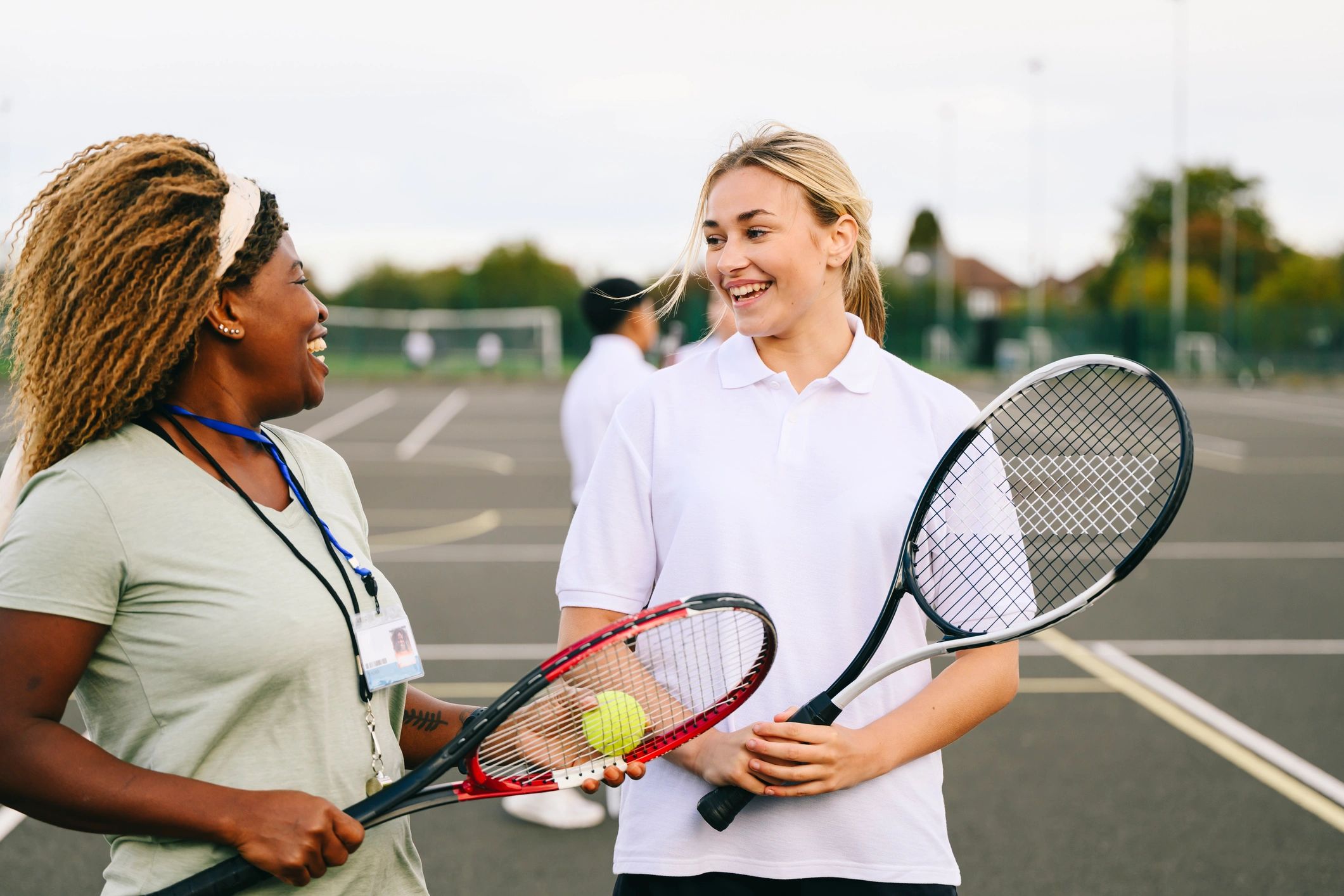Teenage girl smiling and talking to PE teacher with tennis racquets outdoors